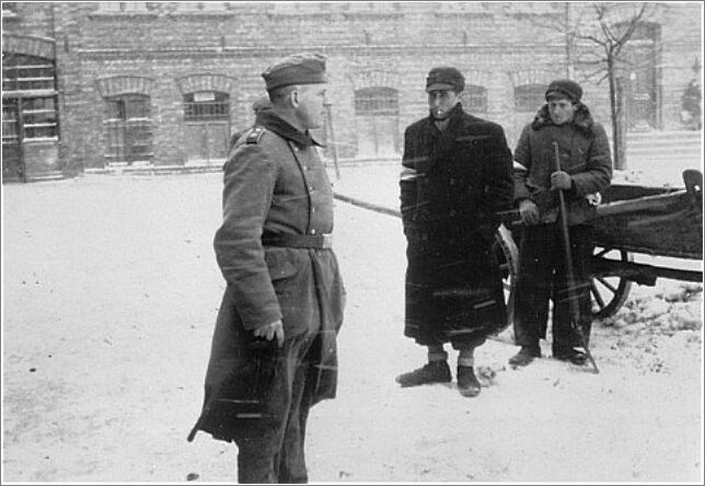 A German soldier and two Jewish man who are clearing snow on a street in Czestochowa ghetto